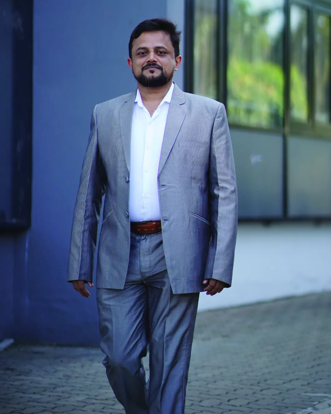 Portrait of a confident man seated indoors wearing a blue suit and casual shoes.