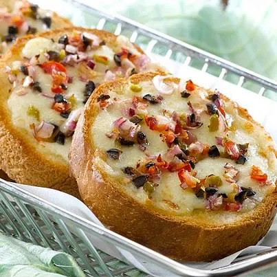 Colorful buffet table featuring mini burgers, pizza, and flowers at an outdoor event.